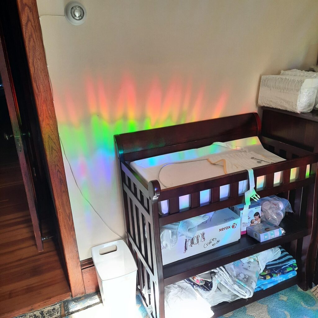 Baby crib in an unlit room witha red, green, and blue rainbow across it